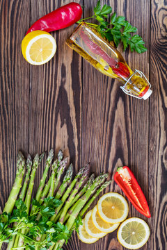 Bottle of olive oil with spices, bunch of fresh green asparagus spears and lemon on a rustic wooden table