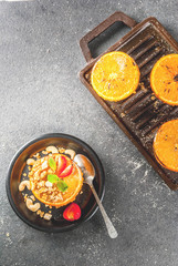 Ideas for a healthy dietary vegan breakfast. Paleo diet. Grilled oranges grapefruits with brown cane sugar, granola, honey, strawberry slices, cashew nuts and mint. On a black stone table. Copy space