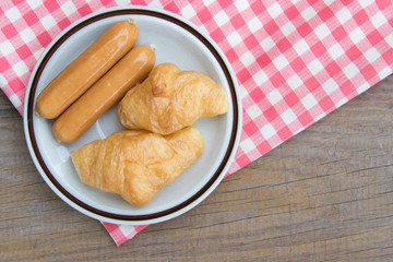 Obraz na płótnie Canvas Close-up Croissant and sausage on plaid red napkin. high angle background