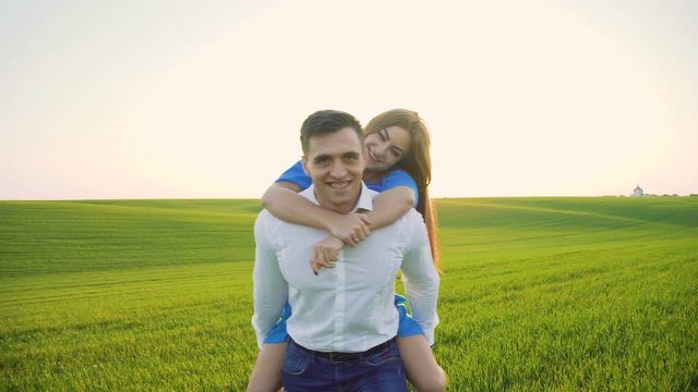 Happy couple on the wheat field. Man carrying his girl on shoulders on sunset