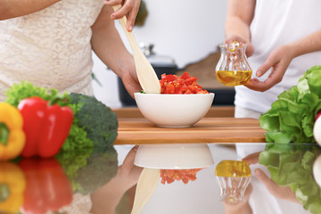 Obraz na płótnie Canvas Closeup of two women are cooking in a kitchen. Friends having fun while preparing fresh salad