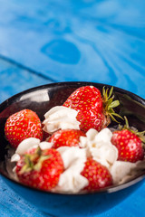 Fresh strawberries in whipped cream above blue wooden background