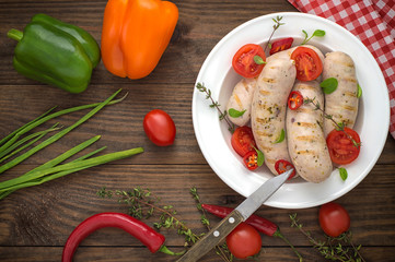 Boiled grilled sausages with cherry tomatoes and chili peppers with greens. Wooden background. Top view. Close-up