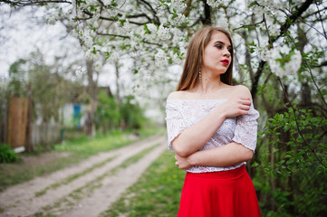 Fototapeta na wymiar Portrait of beautiful girl with red lips at spring blossom garden, wear on red dress and white blouse.