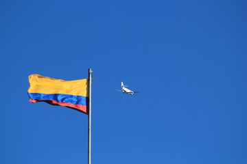 Bandera de Colombia en firmamento azul con avión.