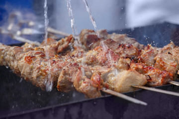 Cooking. Pork meat roasted on a spit. Meat is watered with water, creating splashes and steam. Closeup. When the aperture is wide open, selective focus.
