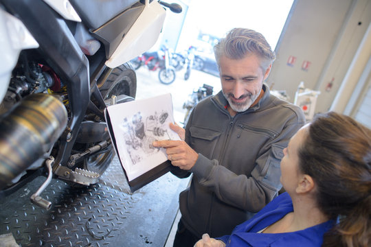 Mechanics looking at exploded view diagram of scooter
