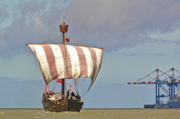 Hanseatic cog under sail with port facilities and cranes