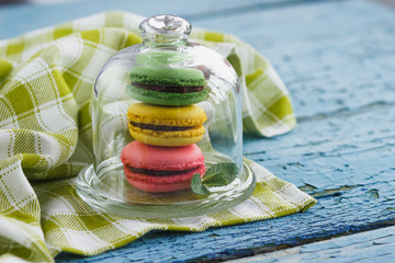 Green, pink and yellow french macarons under the glass on the wooden boards