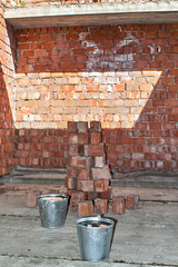 Pile of Bricks by an Old Brick Wall taken by an old building in St. Petersburg. Metal buckets on the construction site.