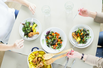 Top view of two young women eating green salads with chiken and potato