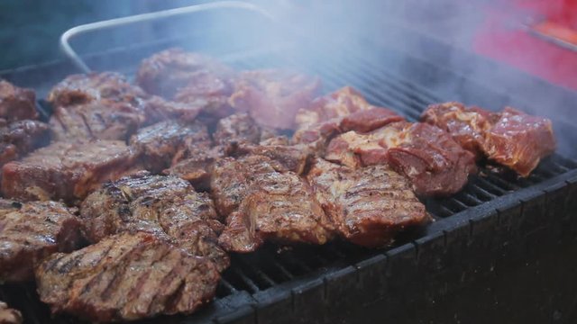 Chef is putting raw meat on grill. Barbecue meat preparing on grill, close up. Mutton or pork grilling. A lot of meat at the street food festival.