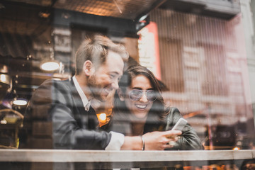 Friends using mobile in a cafe. Couple of lovers having a good time with the cell phone.