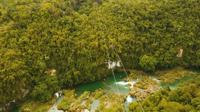 People have fun a zip line through a canyon with a river in the rainforest jungle. Aerial view, tourist attraction at the zipline attraction in the jungle on the island of Bohol. 4K video. Travel