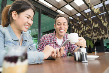 Asian young woman and old man are enjoy with smartphone at coffee shop. Casual meeting outside office concept. A Girl is teaching technology for her father. Funny and hapyy moment.