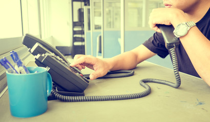 businessman dialing voip phone in the office, keyboard and monitor detail in the background with vintage color tone effect
