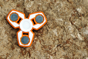 White and Orange fidget SPINNER stress relieving toy on stone background. Israel MAY-13-2017