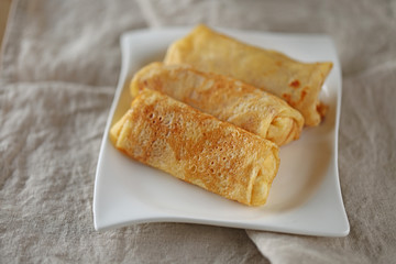 Pancakes stuffed on a white plate on a linen natural napkin.  Breakfast in eco style 