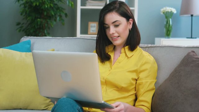Young woman using laptop for chating on internet in skype with friends, family, boyfriend, siting on sofa in the living room.