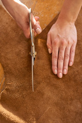 Female artisan cutting brown leather with scissors close up