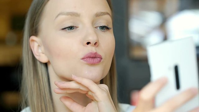 Beautiful, young girl doing selfies on smartphone and checking them

