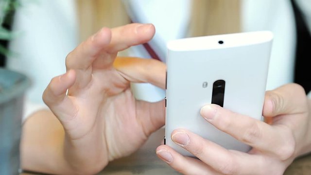 Girl holding white smartphone and browsing internet on it
