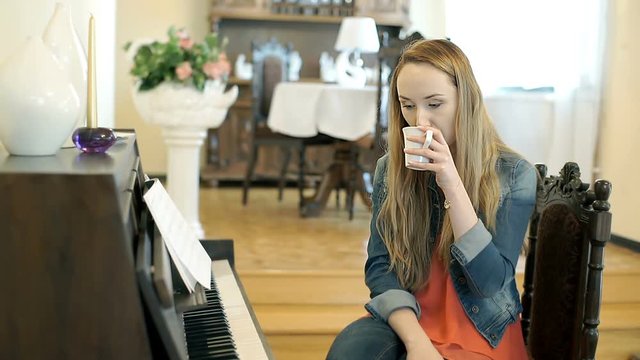 Relaxed girl playing the piano and drinking coffee
