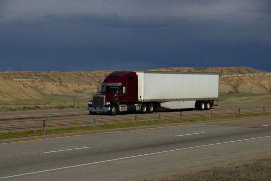 A dark red or Maroon freightliner semi tractor pulls a white trailer down rural Interstate 80 in Wyoming on May 4th, 2017,
