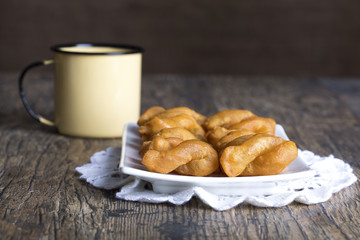 Metal mug full of coffee and a plate of koeksisters on brown wood
