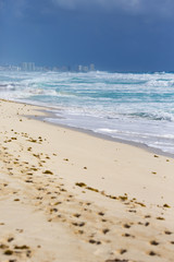 Beach view. Very long sand beach on the shores of the Caribbean sea. Sunny day, no people. City buildings on the background. 