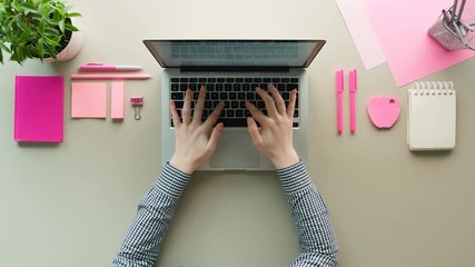 Woman using laptop computer on grey table background with pink details. Female hands typing on the laptop keyboard. Top view - Powered by Adobe