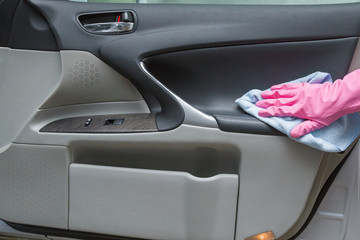 Hand in rubber protective glove with rag cleaning a dusty car interior's door. Early spring cleaning or regular clean up.