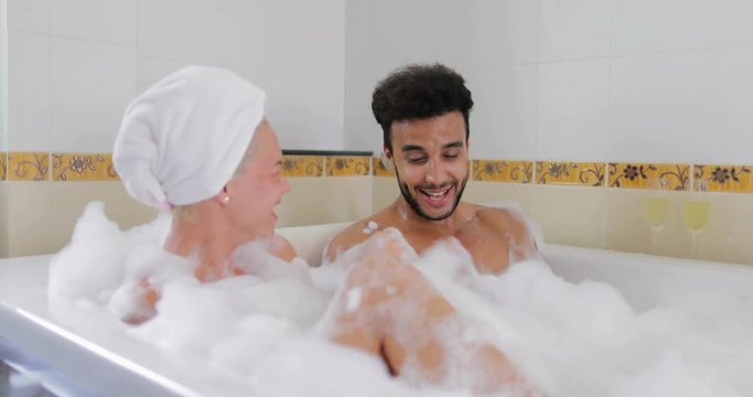 Young Couple Relaxing In Bath Together Blowing Foam, Man And Woman Lover Enjoy Spa At Home Slow Motion 60