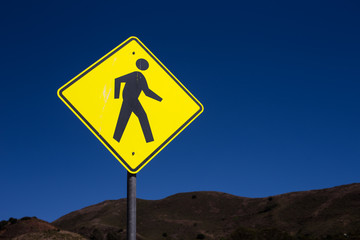Yellow pedestrian caution sign at crossing way and intersection with blue sky background for safety transportation and people in the city
