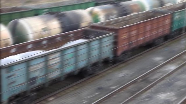 Blurred cargo train arriving at railway station. Wagons moving while oil cisterns standing. Empty railroad at the front. Transportation of construction materials. Industrial scene.