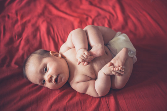 Cute baby in diaper on red bedsheet