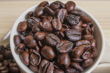 Roasted coffee beans in white cup on wood table