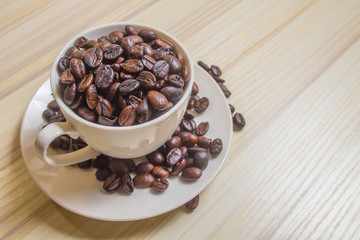 Roasted coffee beans in white cup on wood table