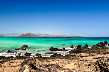 Stunning view of the islands of Lobos and Lanzarote seen from Corralejo Beach (Grandes Playas de Corralejo) on Fuerteventura, Canary Islands, Spain, Europe. Beautiful rocks in the foreground.