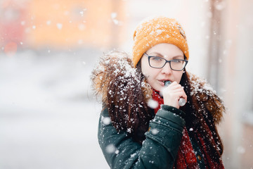 Close-up of an Ecig vaping girl holding a modern mouthpiece of an e-cigarette device in the hands of a vape. Smokes nicotine. Weather of the winter, snow. girl is warmly dressed.vaping