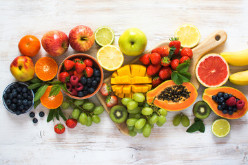 Fototapeta na wymiar Above view of rainbow colored fruits, strawberries, blueberries, mango, orange, grapefruit, banana, apple, grapes, kiwis on the white background, copy space for text, selective focus