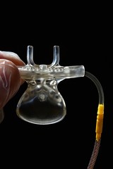 Upper side of sidestream capnography nose and mouth element held in doctor lef hand in glove on dark background