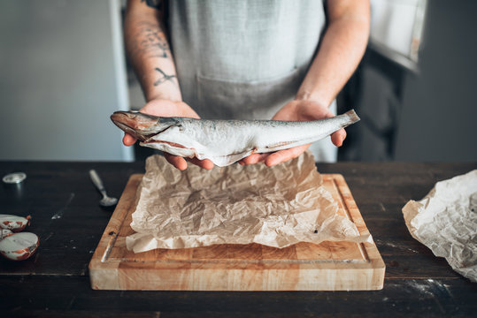 Chef hands holds raw fish over cutting board
