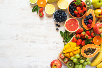 Above view of colorful fruits, strawberries, blueberries, mango, orange, grapefruit, banana, apple, grapes, kiwis on the white background, copy space for text, selective focus