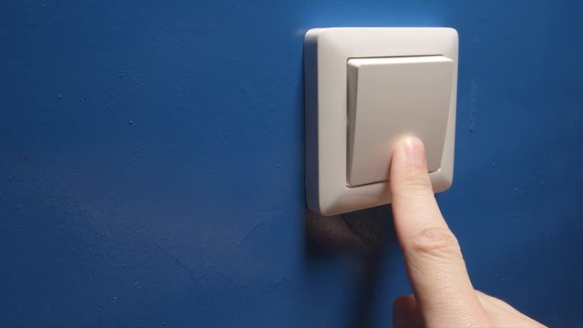 Human hand turn off a power button on a blue wall - side view