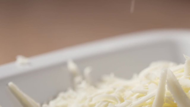 Slow motion slide shot of grated pizza mozzarella cheese falls in plate, 180fps prores footage