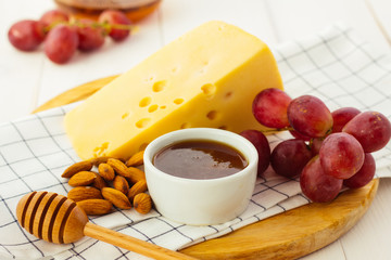 Cheese, almond, grapes and honey on wooden plate