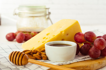 Cheese, almond, grapes and honey on wooden plate