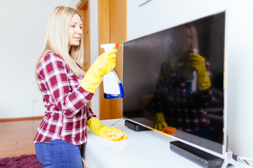 Fototapeta na wymiar Beautiful young smiling woman cleaning TV with microfiber cloth. 