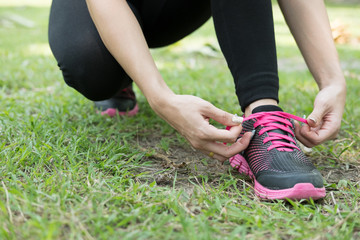 Urban athlete woman tying running shoe laces. Female sport fitness runner getting ready for jogging outdoors on forest path in city park